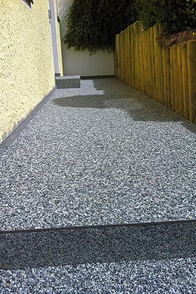 Grauer Steinteppich auf Gartenweg mit Holzzaun